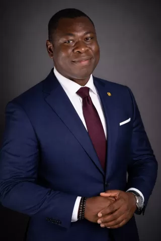 A professional head-and-shoulders portrait of a male academic staff member in a formal suit, facing the camera with a neutral, professional expression against a plain background.